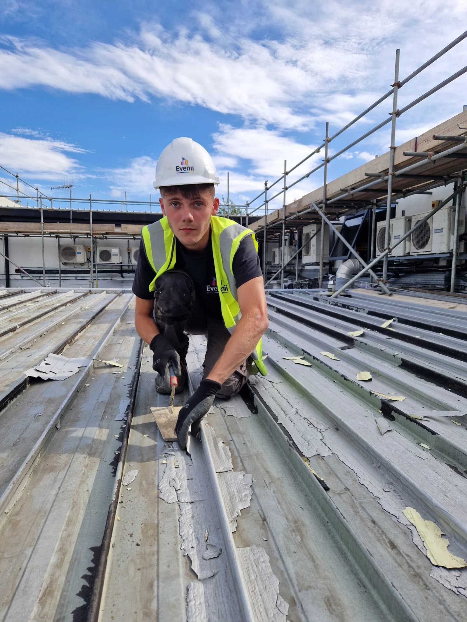 A roofer in branded hi-vis and harness working on a commercial roof in the North East